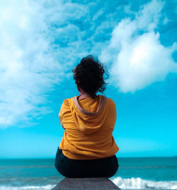 Rear view of woman sitting by sea against sky