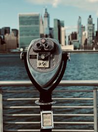 Close-up of coin-operated binoculars against river in city