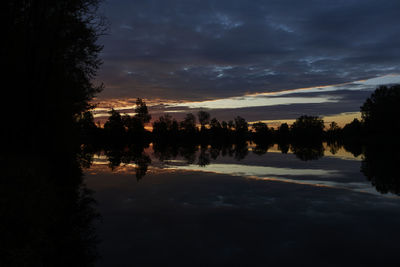 Silhouette trees by lake against sky during sunset