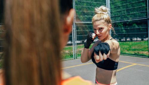 Portrait of female athlete exercising with friend on court against fence