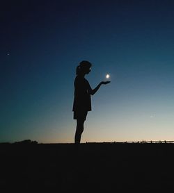 Optical illusion of teenage girl holding moon at night