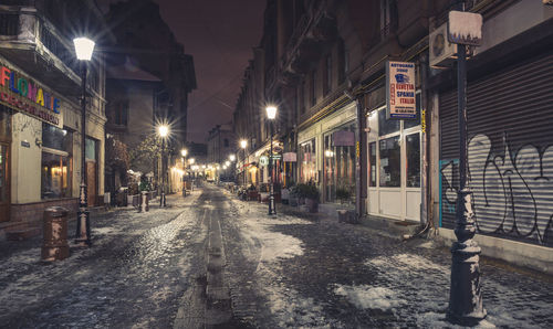 Illuminated street amidst buildings in city at night during winter