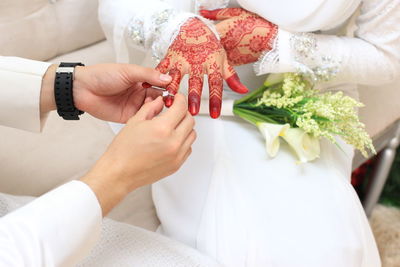 Midsection of groom putting ring in bride finger sitting on sofa during wedding