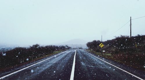 Road by railroad tracks against clear sky during winter