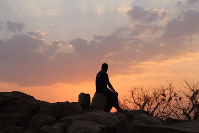 Silhouette man sitting on rock against sky during sunset