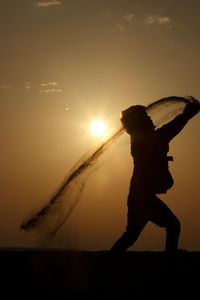 Silhouette boy throwing sand against sky during sunset