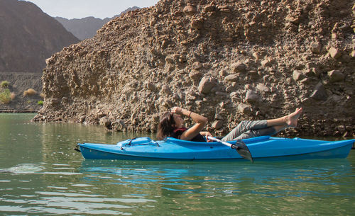 Woman relaxing in kayak by rock formation at river