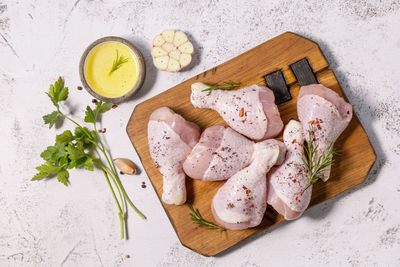 Raw fresh chicken drumsticks with spices on a woden cutting board on a stone countertop. 