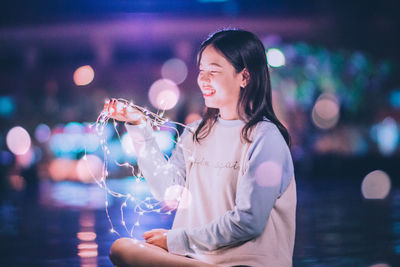 Close-up of smiling young woman holding illuminated while standing outdoors