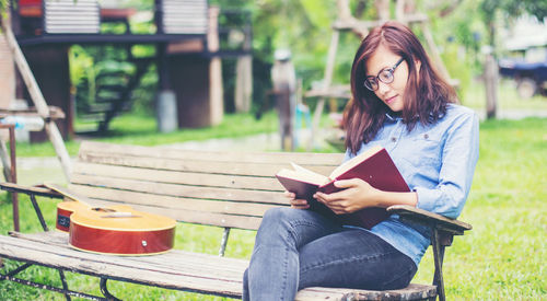 Young woman reading book while sitting on seat