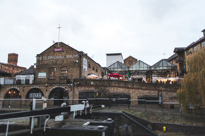 Bridge over canal by buildings against sky in city