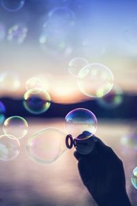 Cropped hand of man making bubbles by lake during sunset