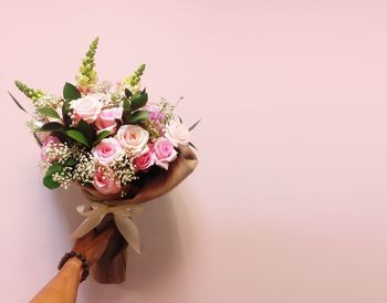 Cropped hand holding bouquet against pink background