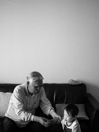 Man assisting grandson in walking while sitting on sofa at home