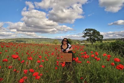 Full length of young woman by poppy field against sky