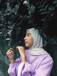 Woman holding pink flower against trees