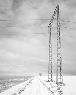 Electricity pylon by road on field against sky