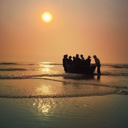 Fishermen standing on sea against sky during sunset