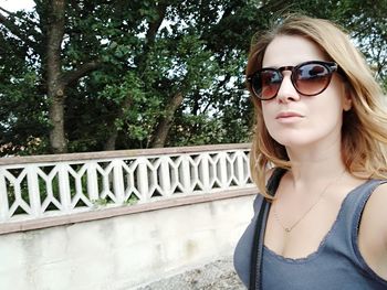 Portrait of young woman wearing sunglasses against trees