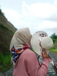 Young woman in hijab holding hat standing on railroad track