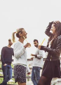 Happy female friends with elderflower drinks enjoying at rooftop party
