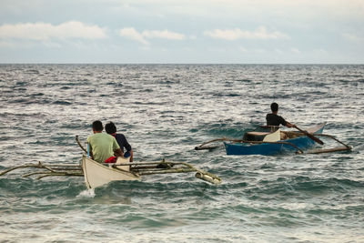 Men on rowing boats in sea against sky
