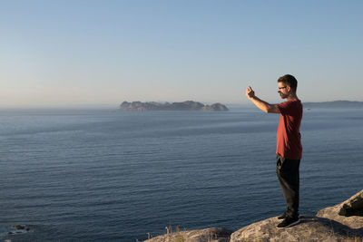 Full length of man standing on rock in sea against clear sky