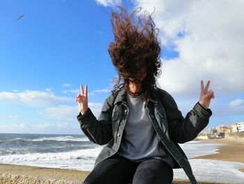 Woman with arms raised at beach against sky