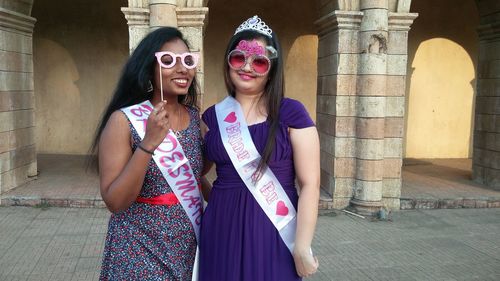 Portrait of smiling females with props while standing against building