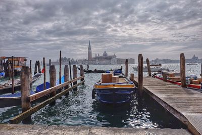 Boats moored at harbor at grand canal against cloudy sky