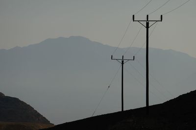 Silhouette power lines on mountain during sunset