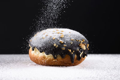 Close-up of powdered sugar falling on donut against black background
