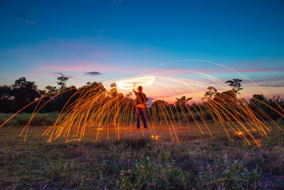 Man spinning wire wools against sky at sunset