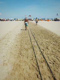 Rear view of men walking on beach against sky