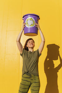 Full length of a smiling young woman standing against yellow wall