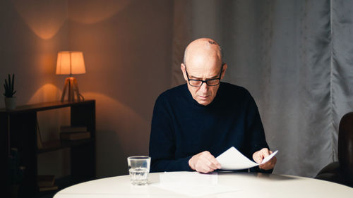 Elderly man sitting at the table reads his electricity and gas bills