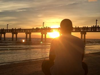 Rear view of man looking at sea against sky during sunset