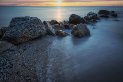 Rocks on beach against sky during sunset