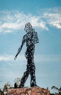 Low angle view of man standing by statue against sky