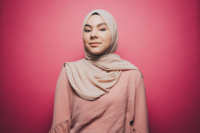 Portrait of confident young woman wearing hijab against pink background
