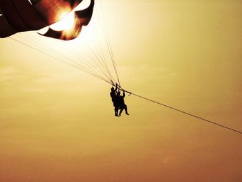 Low angle view of man holding rope against sky during sunset