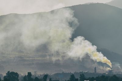 Smoke emitting from mountain against sky