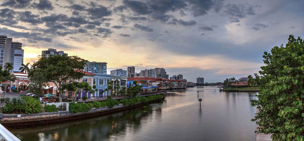 River amidst buildings in city against sky at sunset