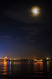 Illuminated city by river against sky at night