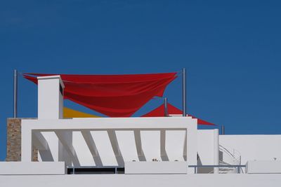 Low angle view of flags against building against clear blue sky