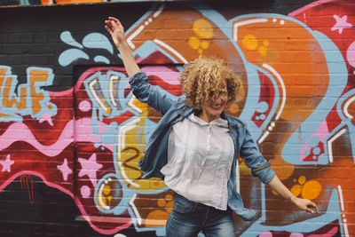 Cheerful woman dancing against graffiti wall