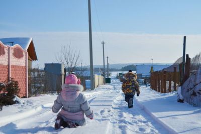 Rear view of kids on snow covered road against sky