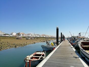 Boats moored at harbor against clear blue sky