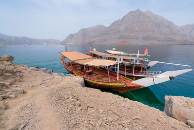 Two traditional arabian dhow boats parked by an island in turquoise fjord on a hazy day.