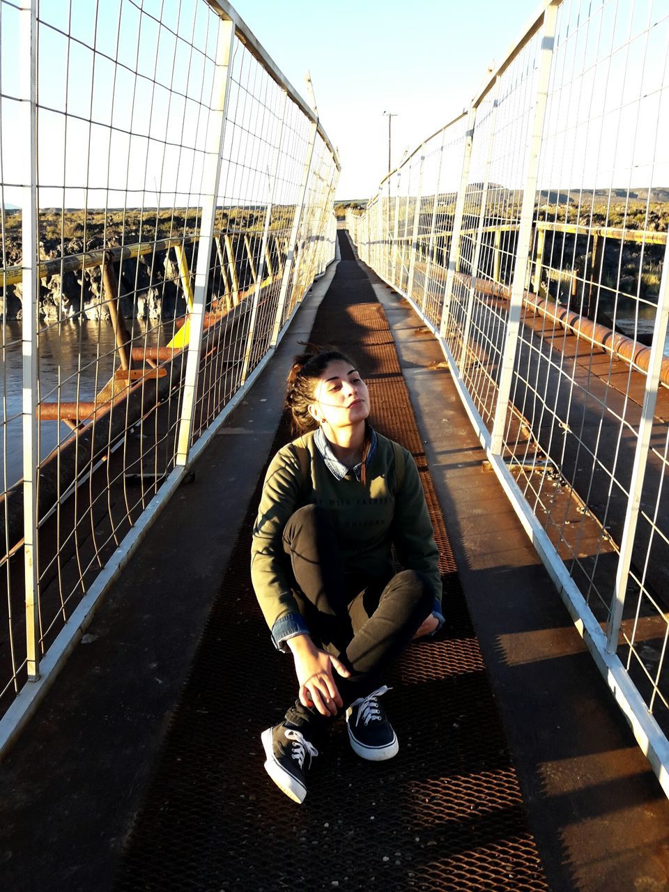 MAN SITTING ON RAILING BY SUSPENSION BRIDGE